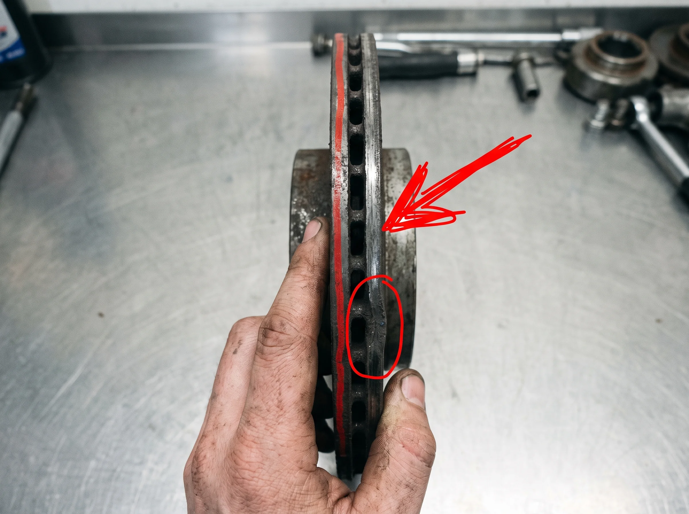 A worn brake disc held edge-on so the lip of wear shows, circled in red marker
