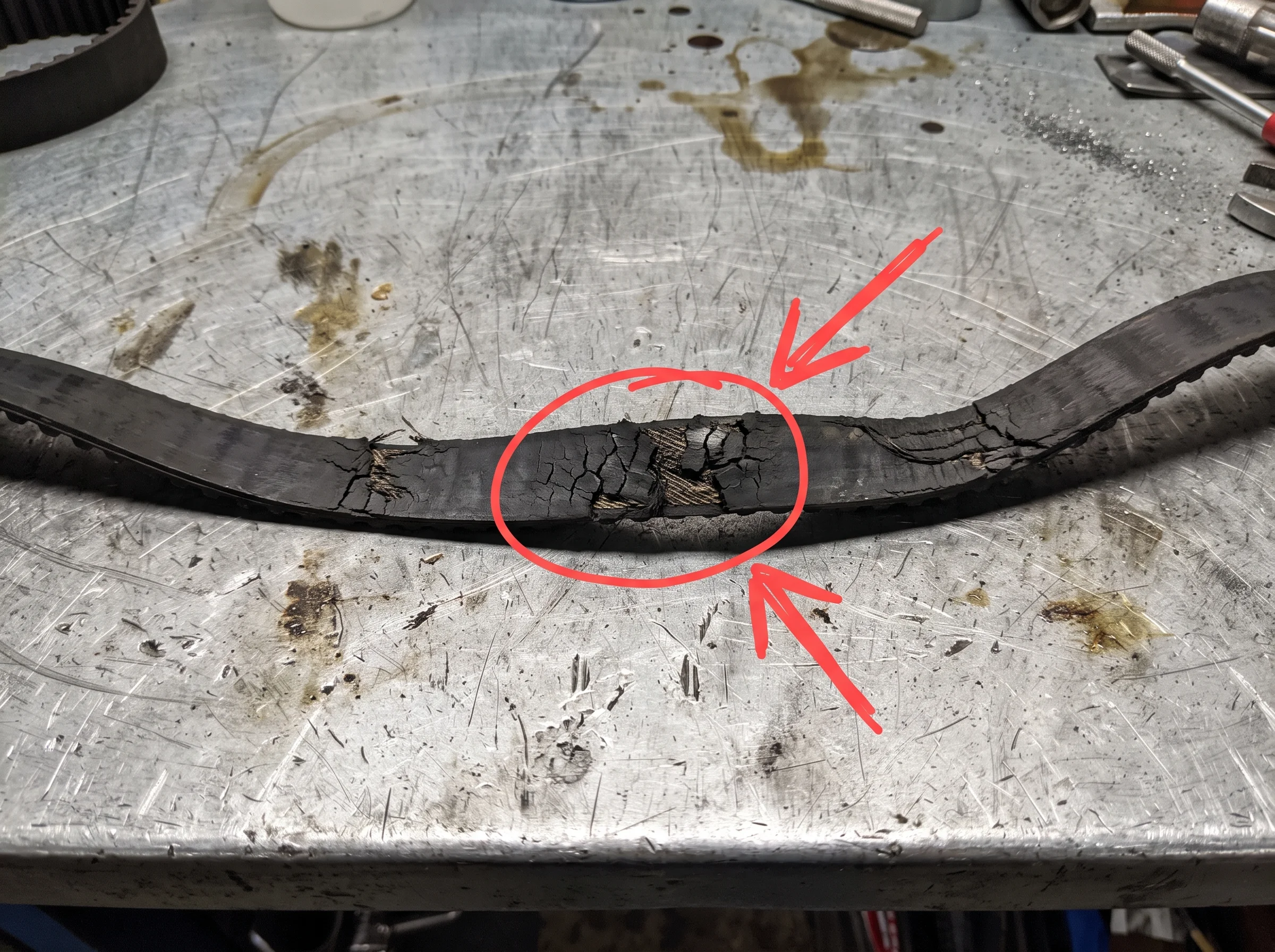 An old timing belt on the bench with cracking across the ribs circled in red marker