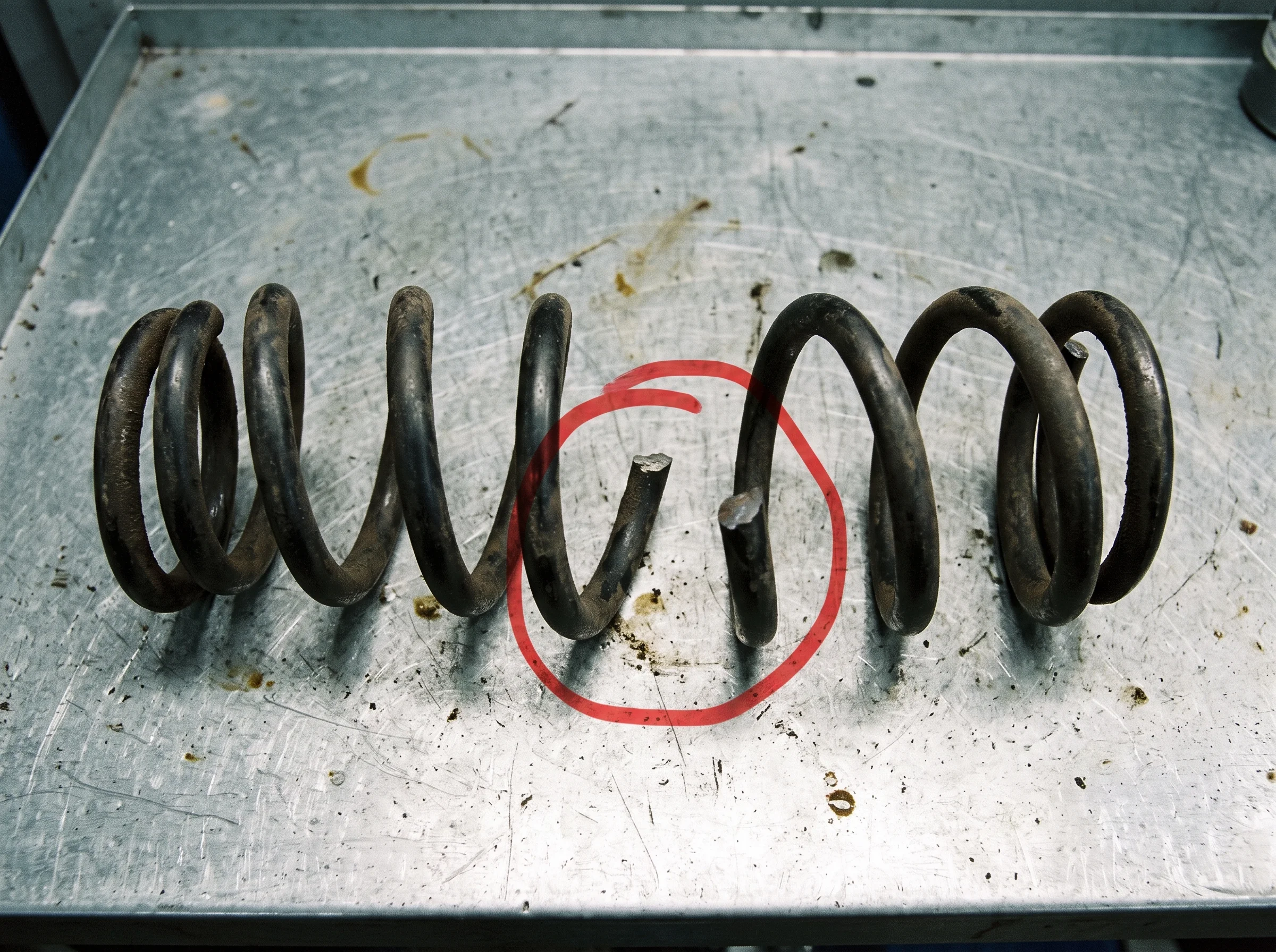 A snapped coil spring on the bench with the fracture circled in red marker